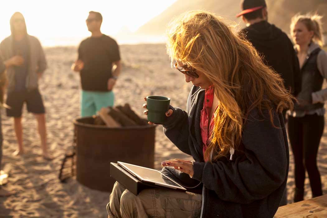 Woman using digital tablet on beach, friends in background